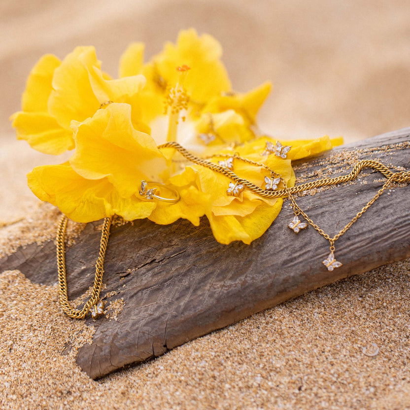 Goldene Kette und Ohrringe mit Schmetterlingsdesign auf gelber Blüte, PURELEI inspiriert.